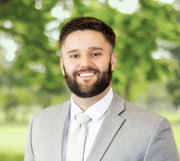 portrait of Trae Pilster, mulat man with dark blonde hair, smiling and wearing light gray blazer, standing outside